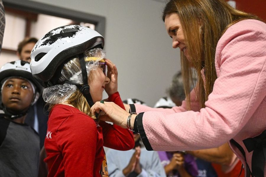 Governor Sanders helps a student put a bike helmet on.